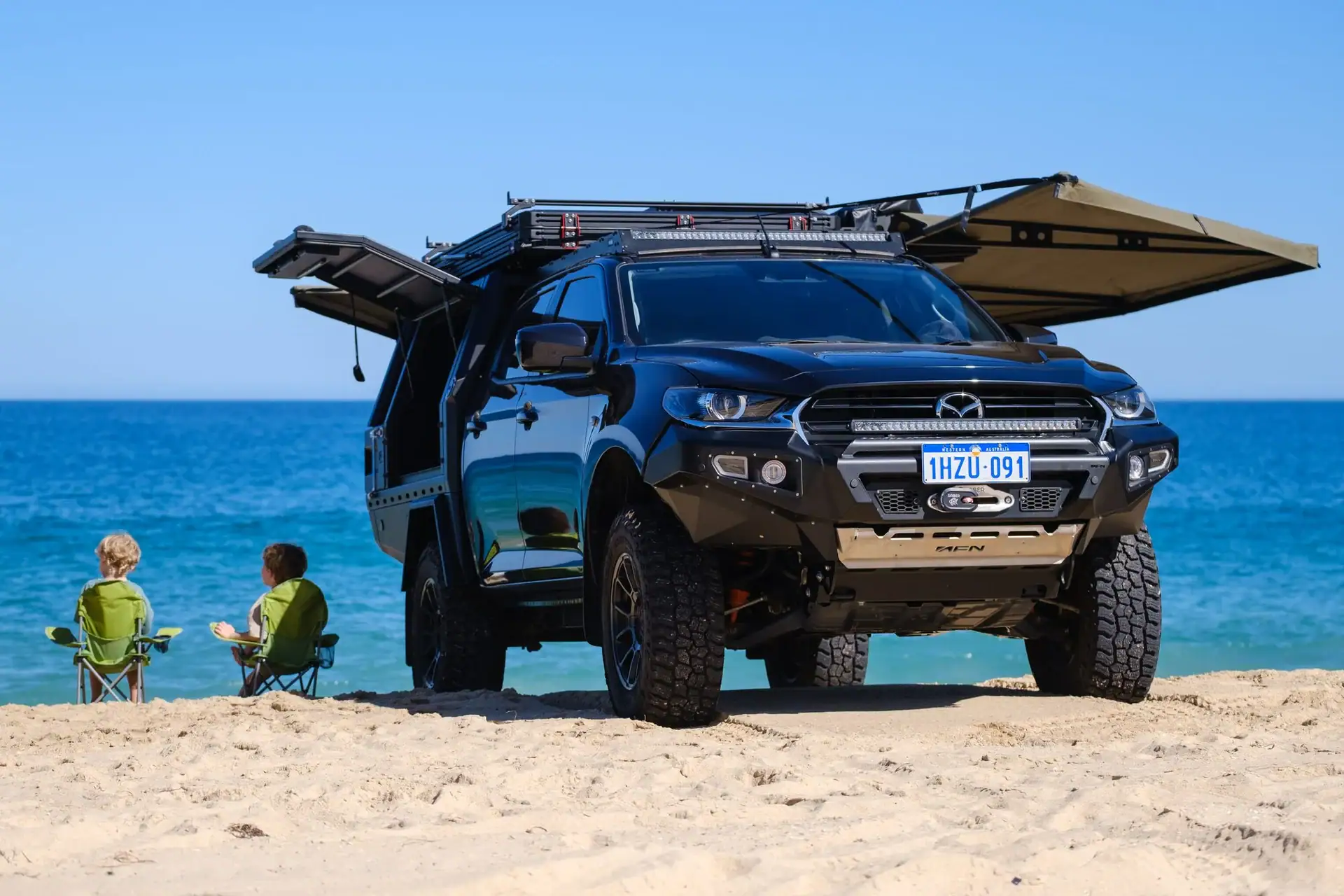 Loaded dual-cab ute on the beach with roof rack, canopy and both awnings deployed